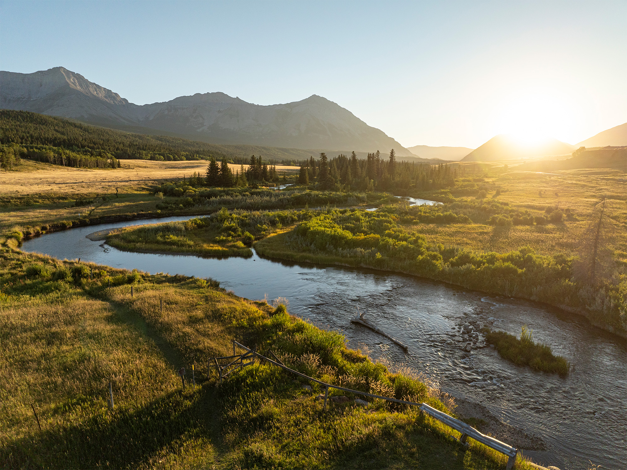 Majestic view of a serene river winding through lush greenery and mountainous terrain in Alberta, Canada, under dramatic clouds.