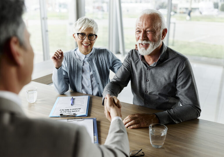 Older couple shaking hands with a man over a desk with documents between them