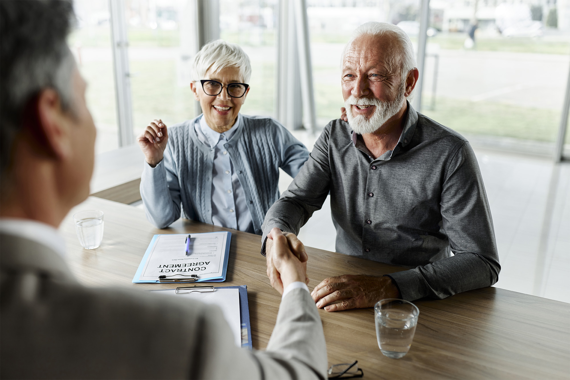 Older couple shaking hands with a man over a desk with documents between them