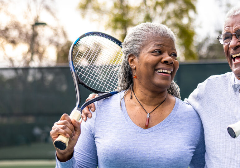 Two elderly people playing tennis outdoors smiling