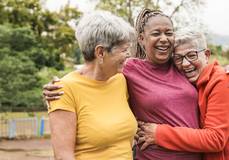 Three women share embrace outside in the sun